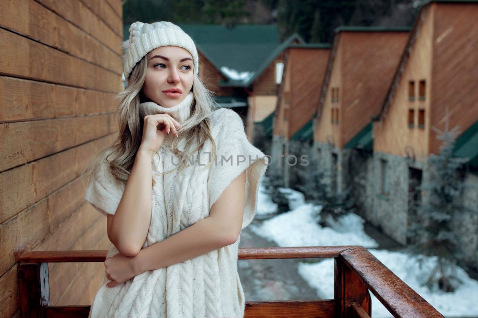 Portrait of a beautiful girl in a white hat and sweater on the street on the balcony. Warm winter clothes.