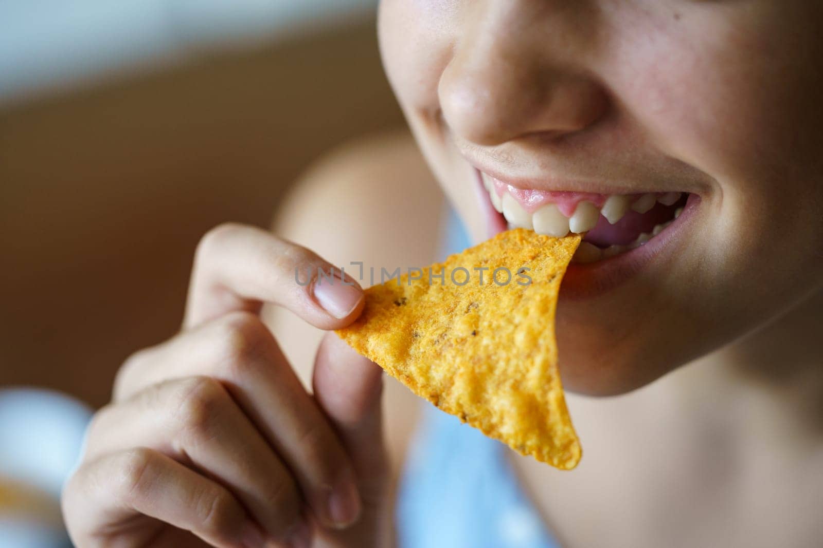 Closeup of crop anonymous young girl smiling while eating spicy Mexican tortilla chip at home