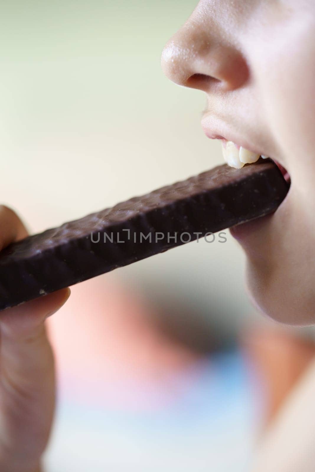 Side view of crop unrecognizable young girl eating chocolate protein bar at home