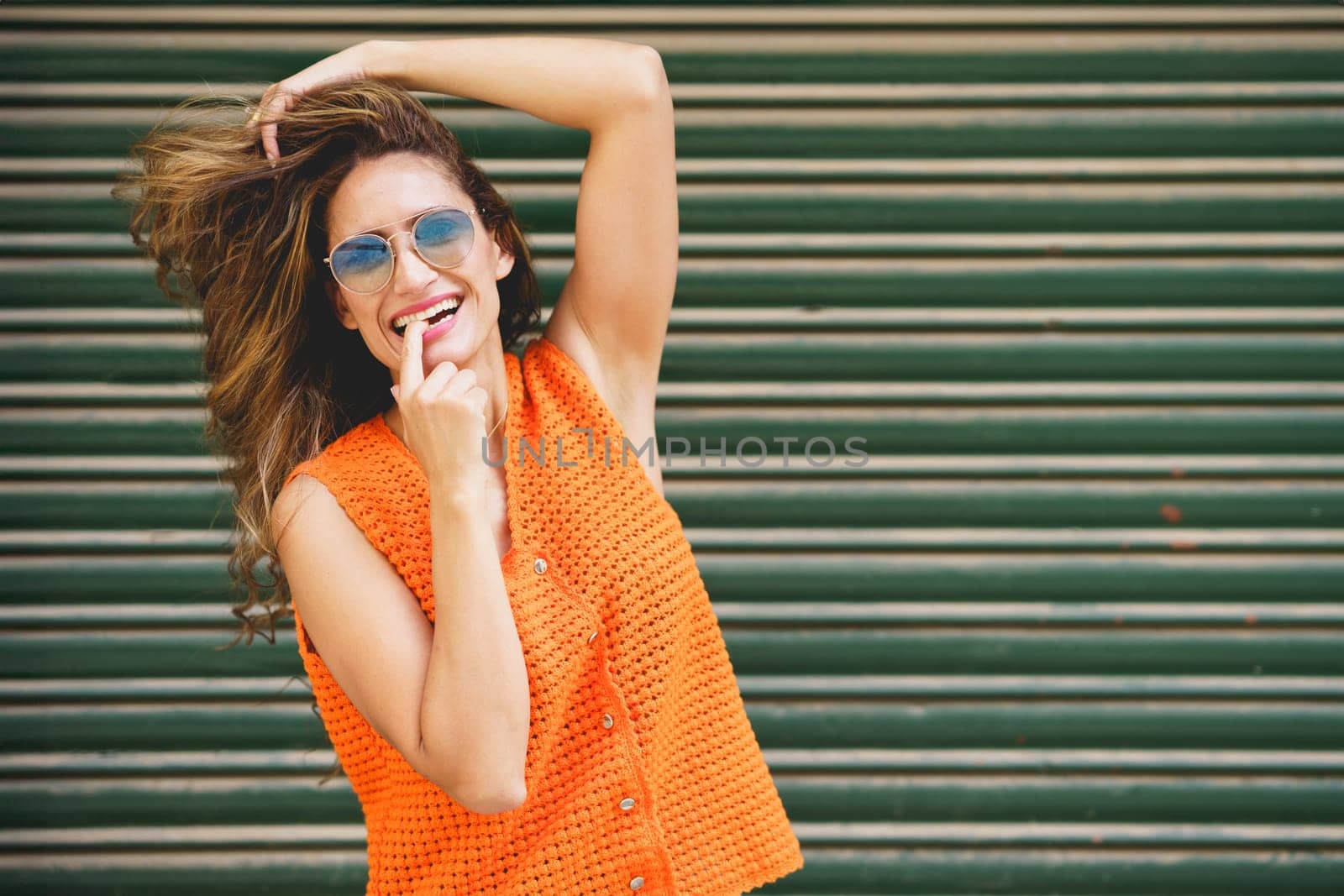 Urban portrait of a cool latin woman with finger on mouth smiling at camera holding her hair