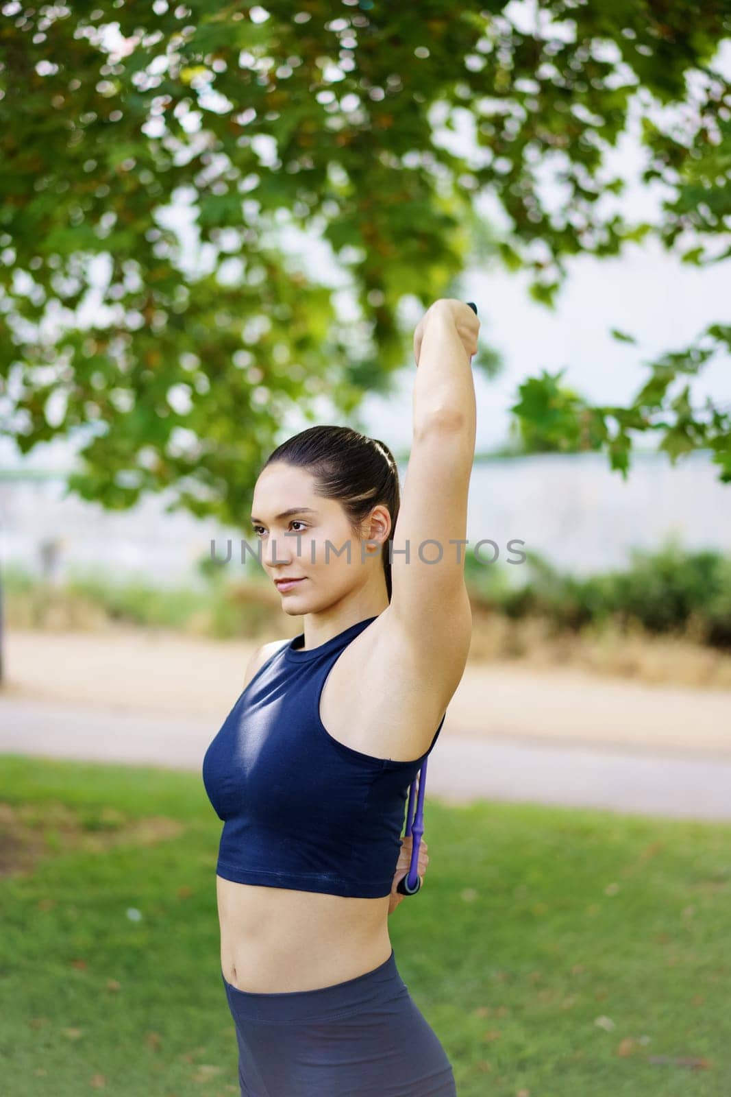 A young woman in athletic attire stretches in the park under sunny skies, promoting fitness and wellbeing in a serene outdoor environment, embracing a healthy and active lifestyle
