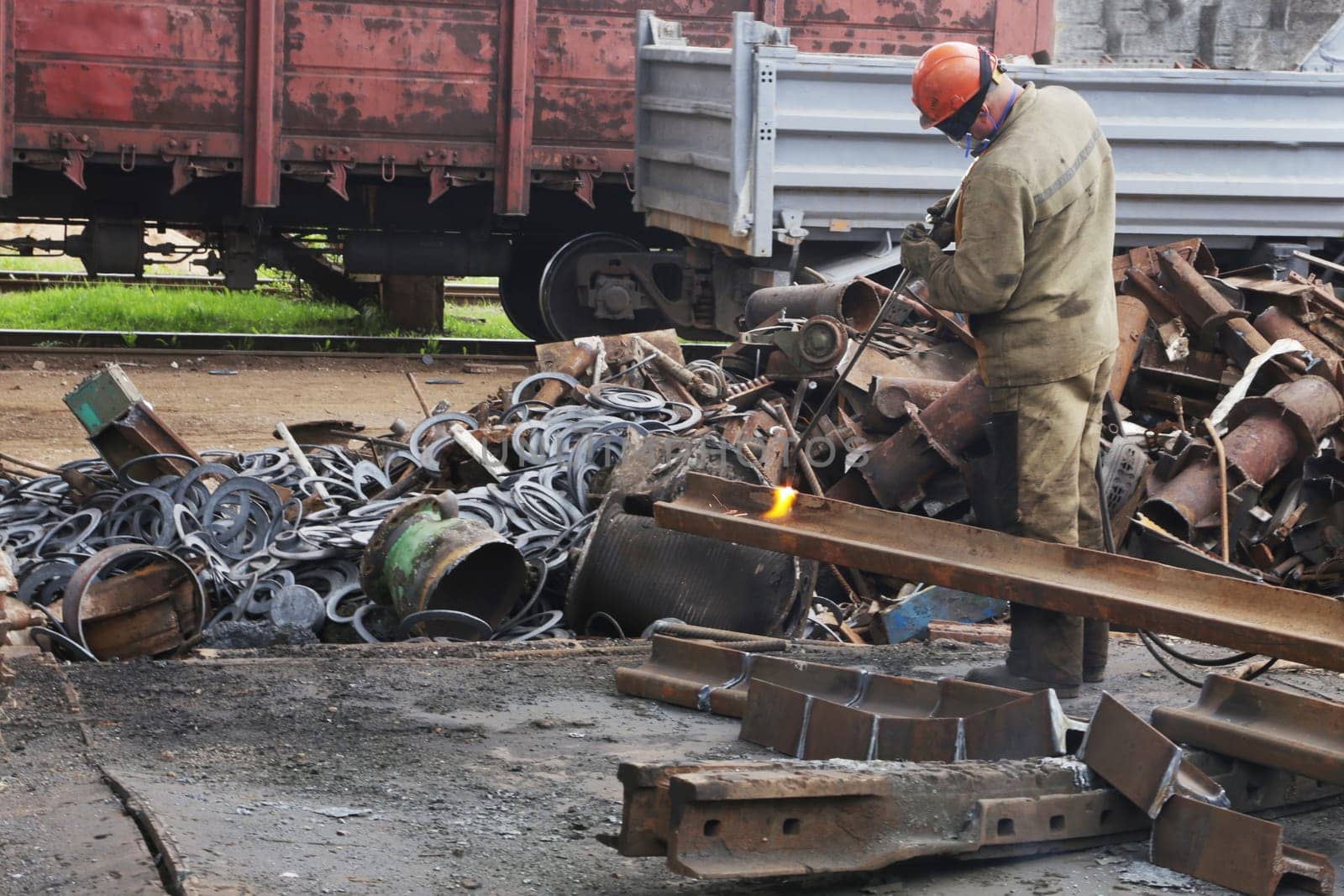 A worker wearing overalls and a helmet operates an autogenous torch to dispose of metal products.