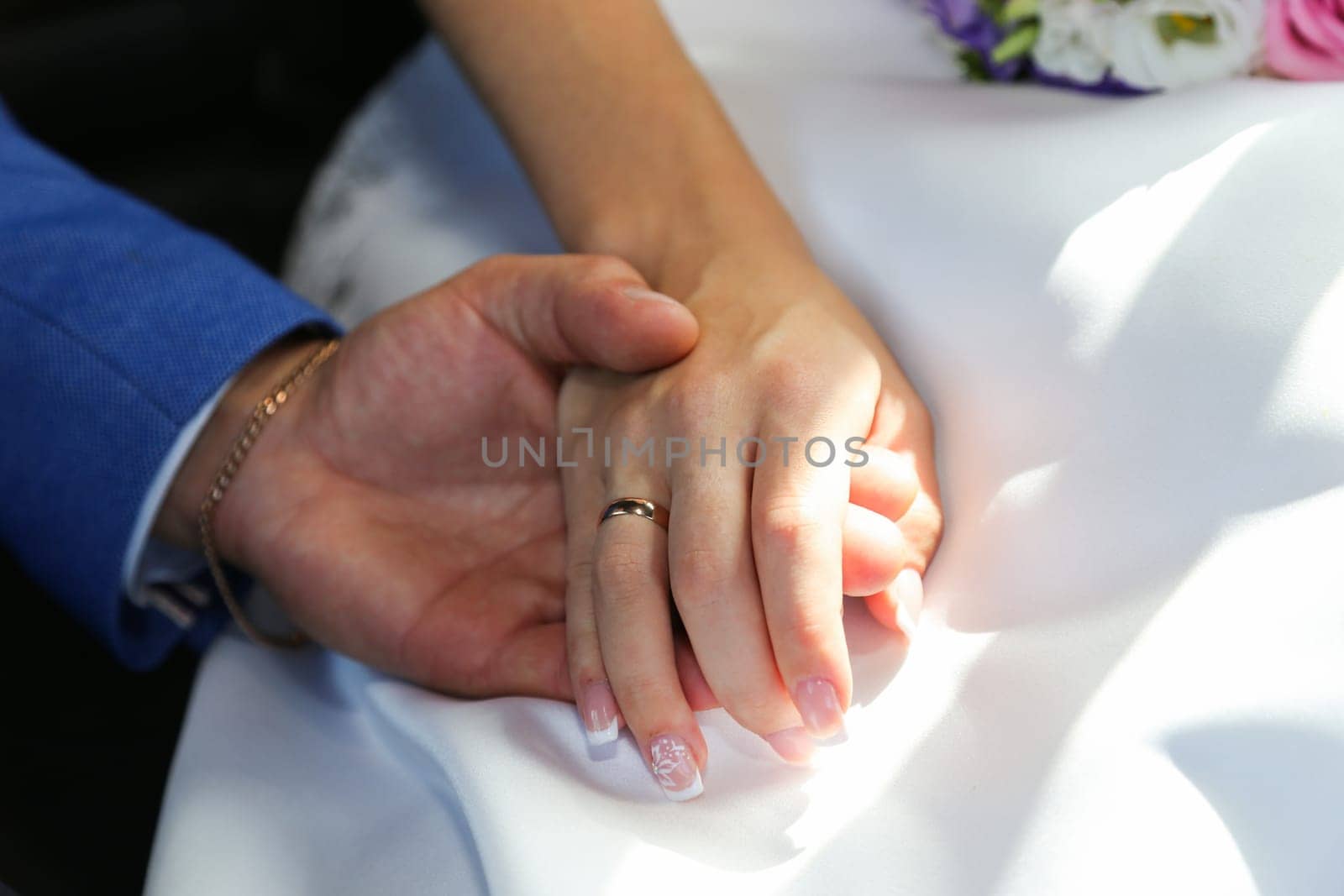 The groom's hand gently takes the bride's hand against the backdrop of the wedding dress. The bride's hand with the wedding ring.