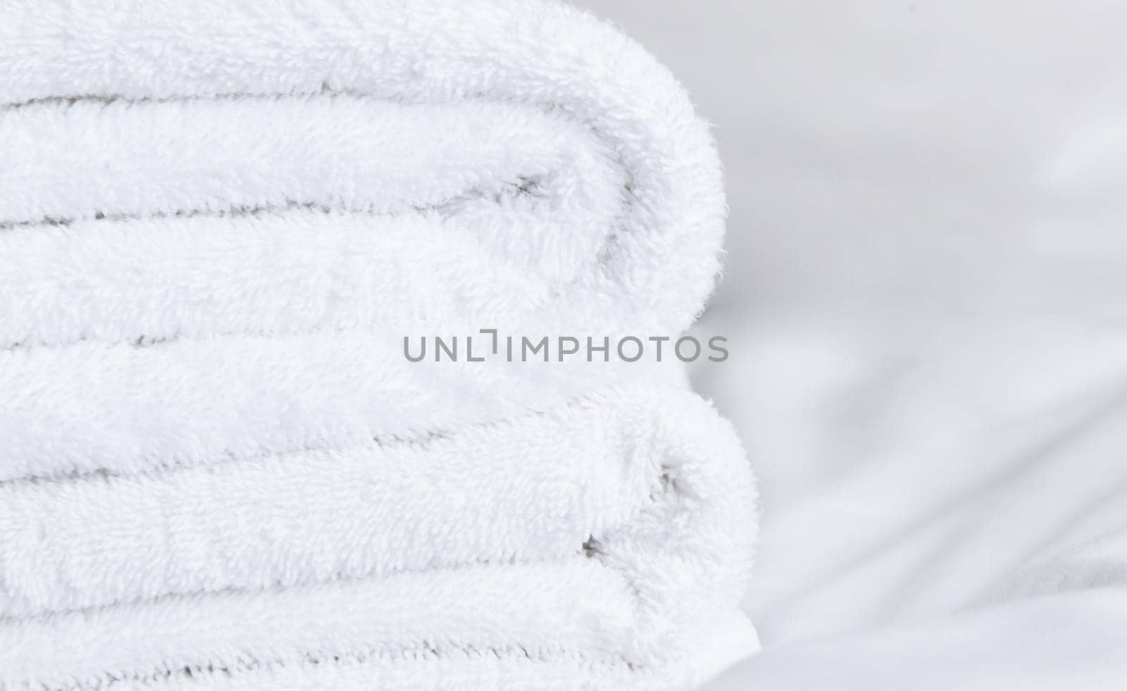 White terry towels stacked on top of each other lie on a white sheet close-up.