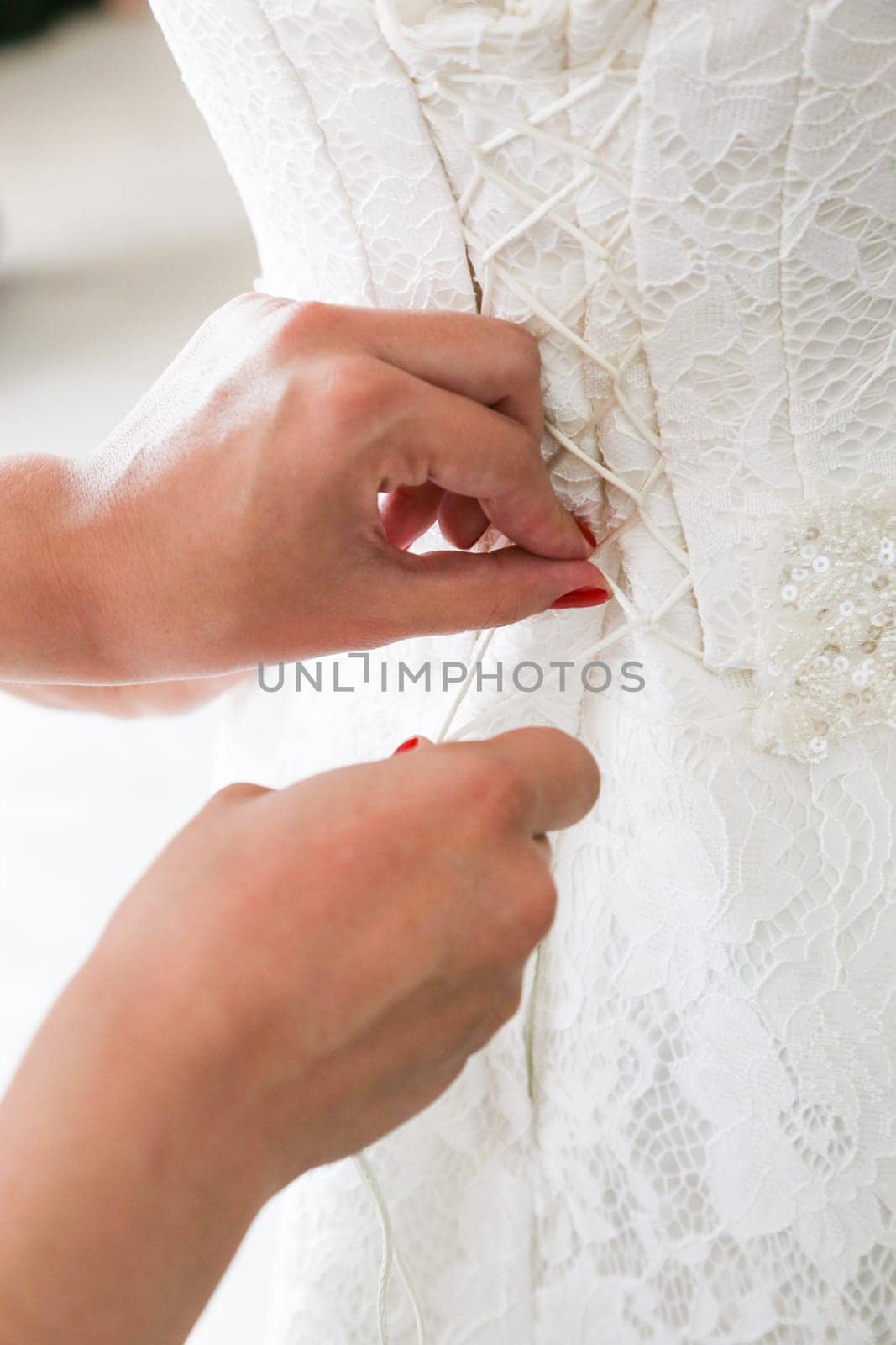 Vertical photo of bridesmaid's hands tying wedding dress laces on back closeup.