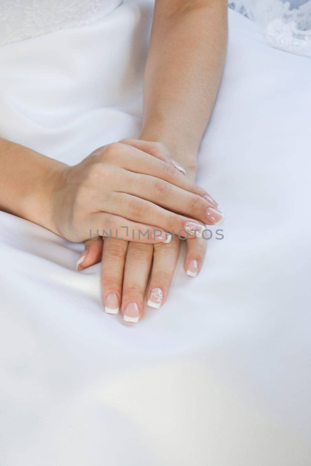 Beautiful young hands lying on a light colored wedding dress, hand on hand. Wedding concept of waiting for the bride.