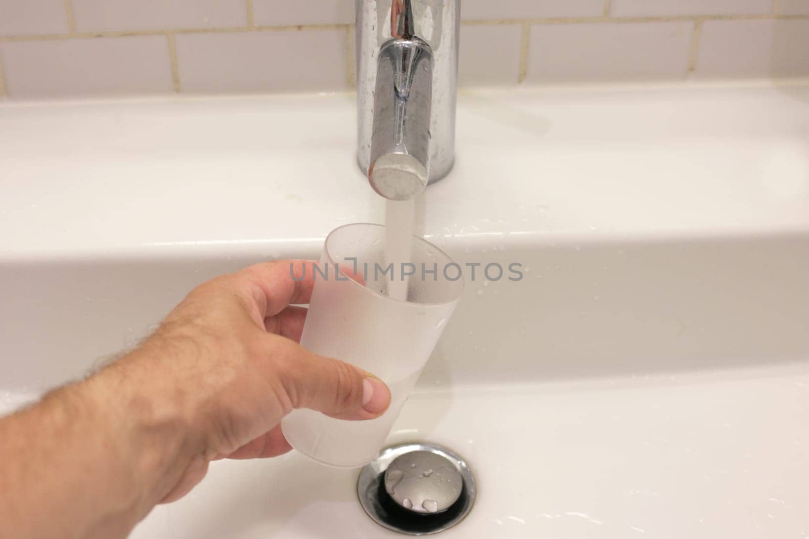 A man's hand pours water from a tap. Water flows from the tap into a glass.