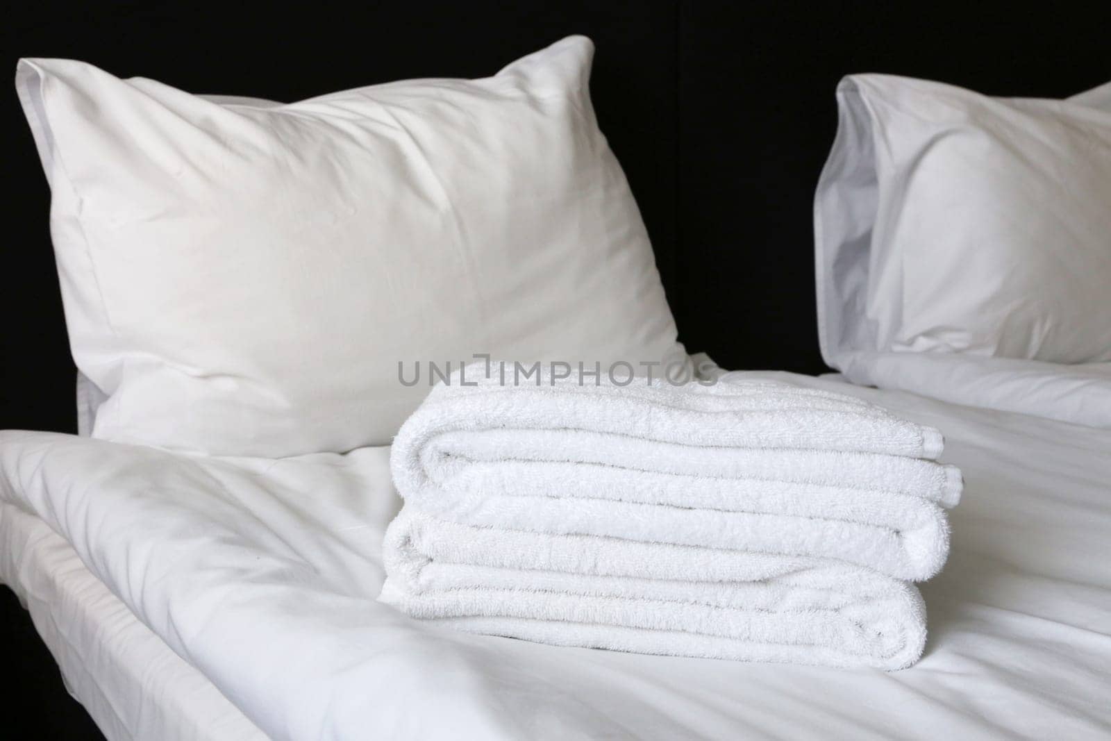 Two pillows on a bed covered with white linen, a sheet, towels. Bedroom in a hotel.