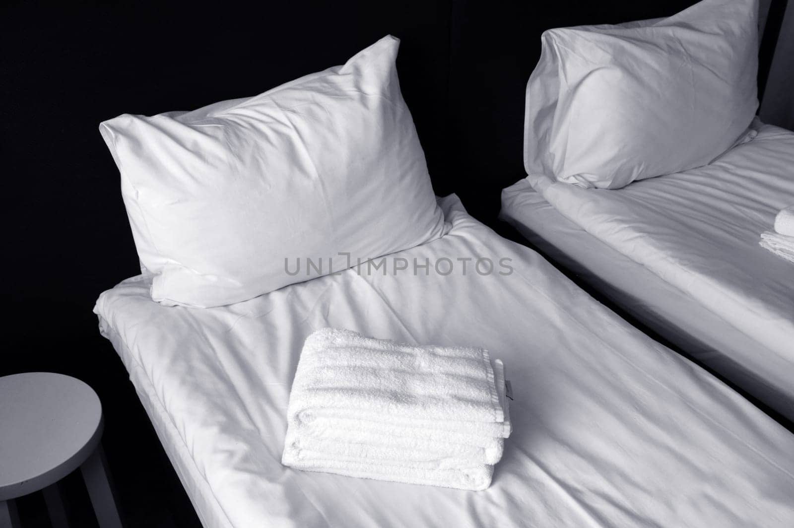 Freshly made beds with white sheets, white pillows, and towels. Fragment of a cozy bedroom.