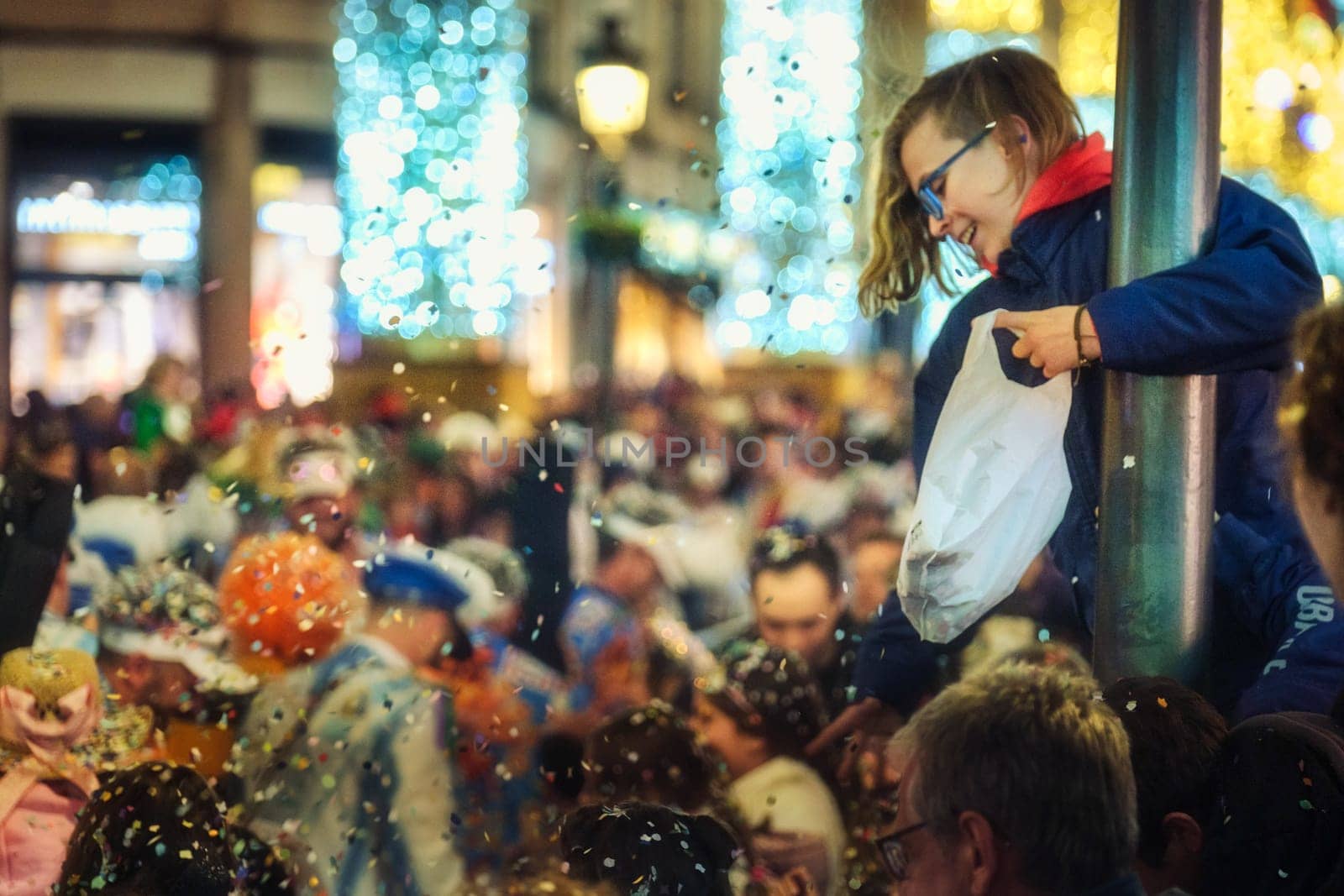 child with glasses holding onto what appears to be a pole or column. festive or celebratory atmosphere. The crowd engaged in some sort of activity that involves the tossing or releasing of these white specks.