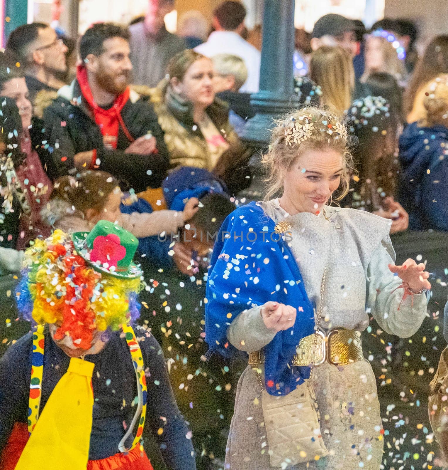 group of people during what appears to be a festive occasion or celebration, as evidenced by the confetti in the air and the cheerful expressions on their faces. In the center is a woman wearing a crown-like accessory on her head and a smile on her face, which suggests she might be part of a special event or ceremony