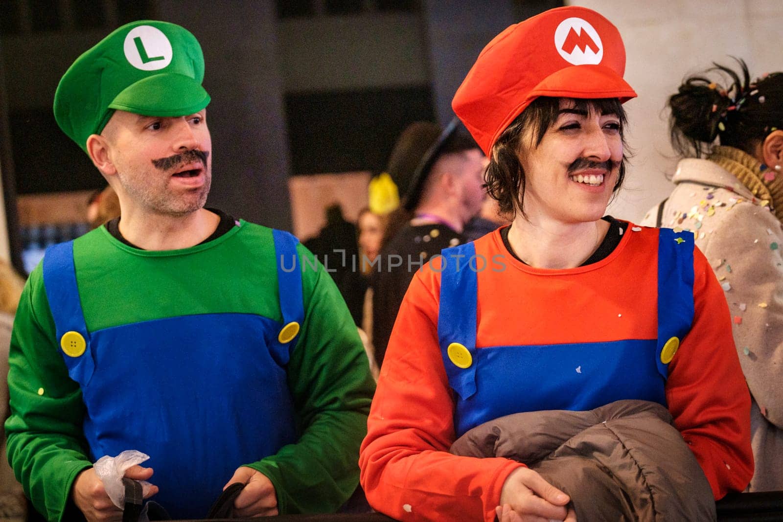 two people dressed up as characters commonly associated with the Mario video game franchise. On the left, someone is dressed in a green shirt, blue overalls, a green hat with an L on it, and a fake mustache, representing the character often known as Mario's brother