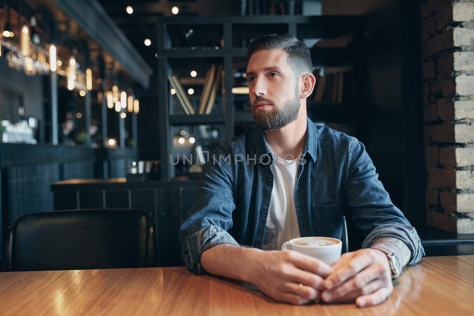 Confident man enjoying a cup of coffee while having work break lunch in modern restaurant, young intelligent man or entrepreneur relaxing in indoors cafe looking pensive