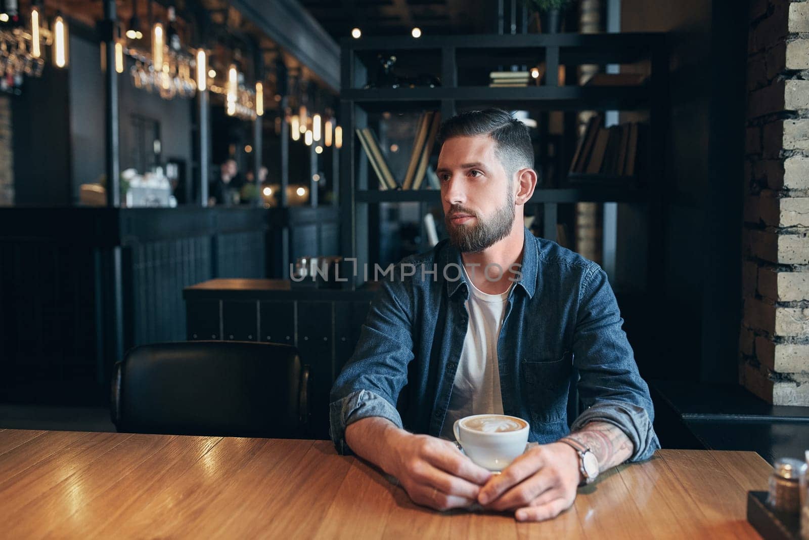 Confident man enjoying a cup of coffee while having work break lunch in modern restaurant, young intelligent man or entrepreneur relaxing in indoors cafe looking pensive