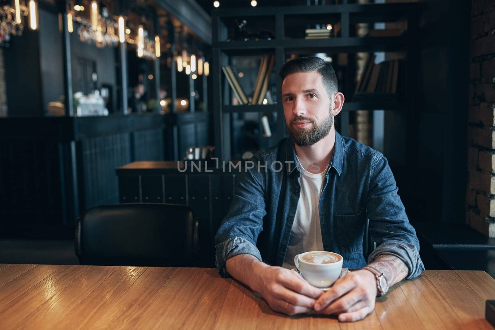 Confident man enjoying a cup of coffee while having work break lunch in modern restaurant, young intelligent man or entrepreneur relaxing in indoors cafe looking pensive