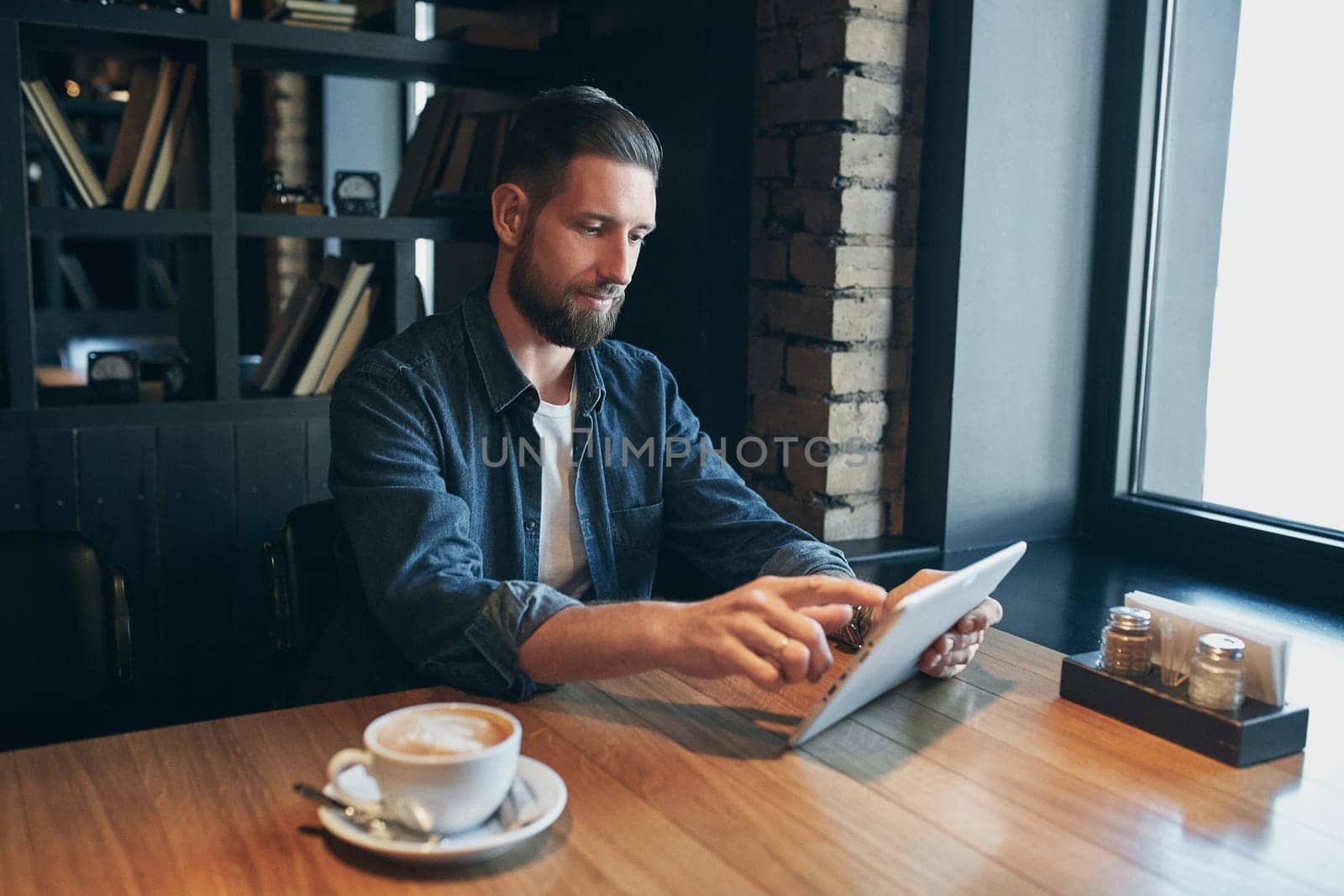 Young man drinking coffee in cafe and using tablet computer. Freelancer. Workplace. Lunch
