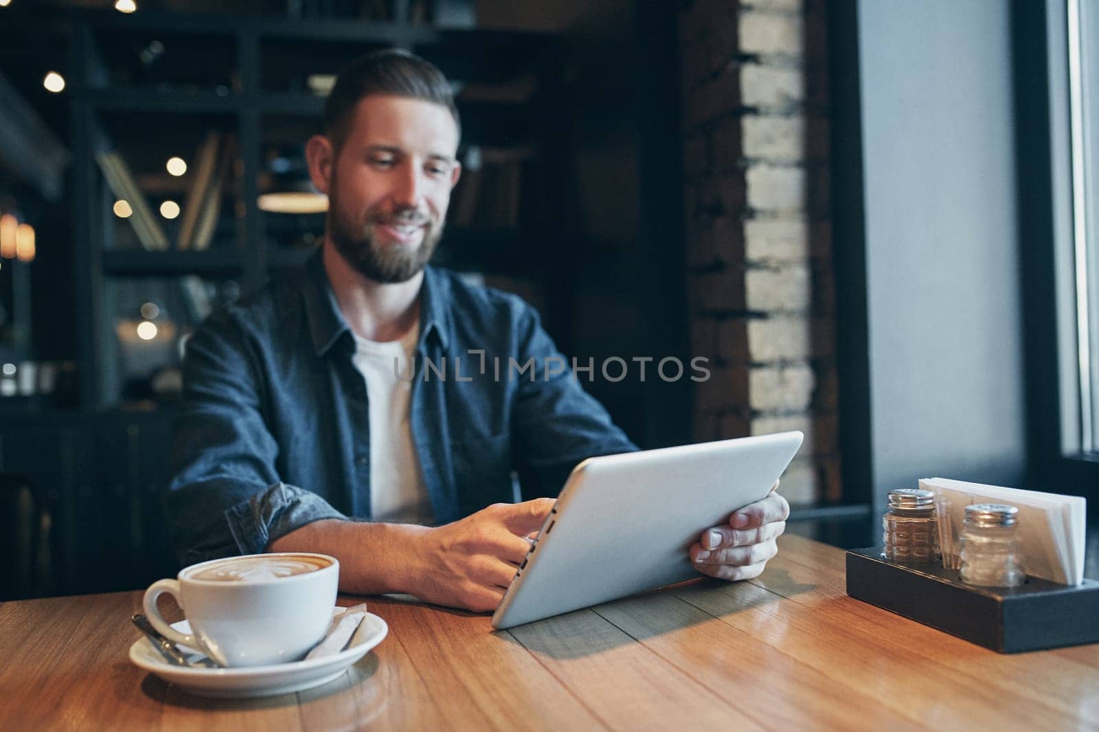 Young man drinking coffee in cafe and using tablet computer by nazarovsergey