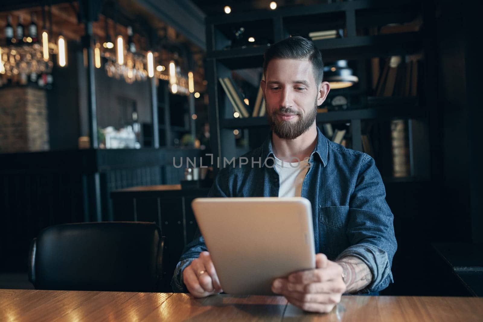 Modern hipster businessman drinking coffee in the city cafe during lunch time and working on tablet. Freelancer