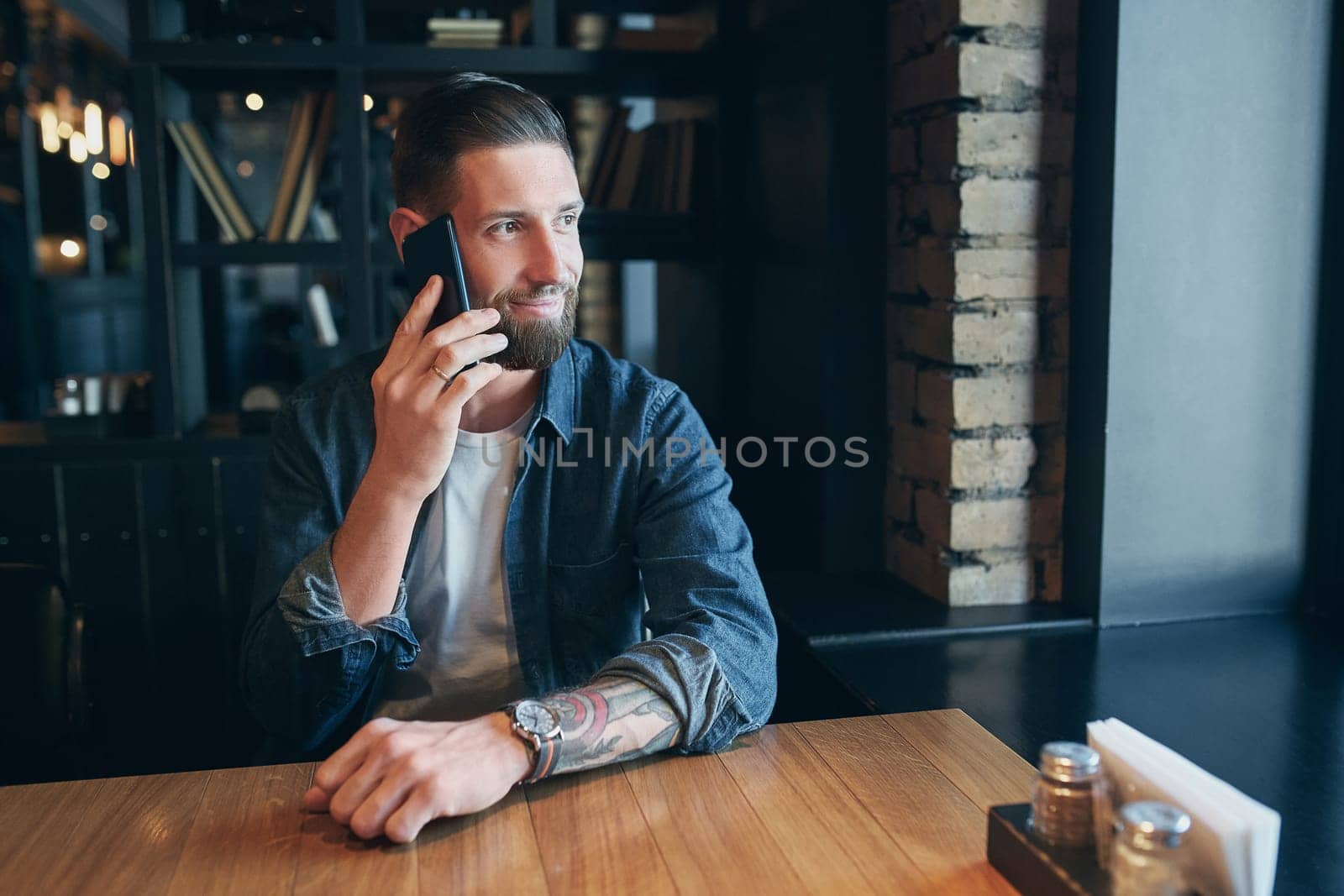 Talking with friends. Confident young man talking on the mobile phone and smiling while sitting in cafe