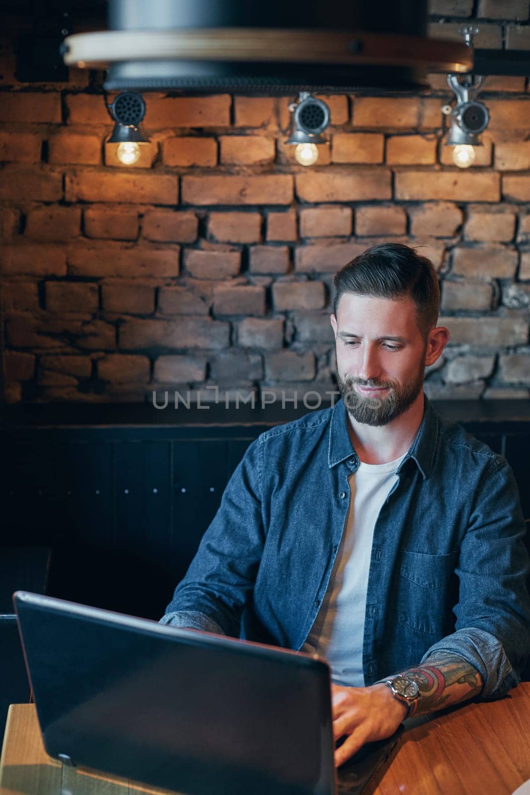 Handsome young man working on laptop while enjoying coffee in cafe by nazarovsergey