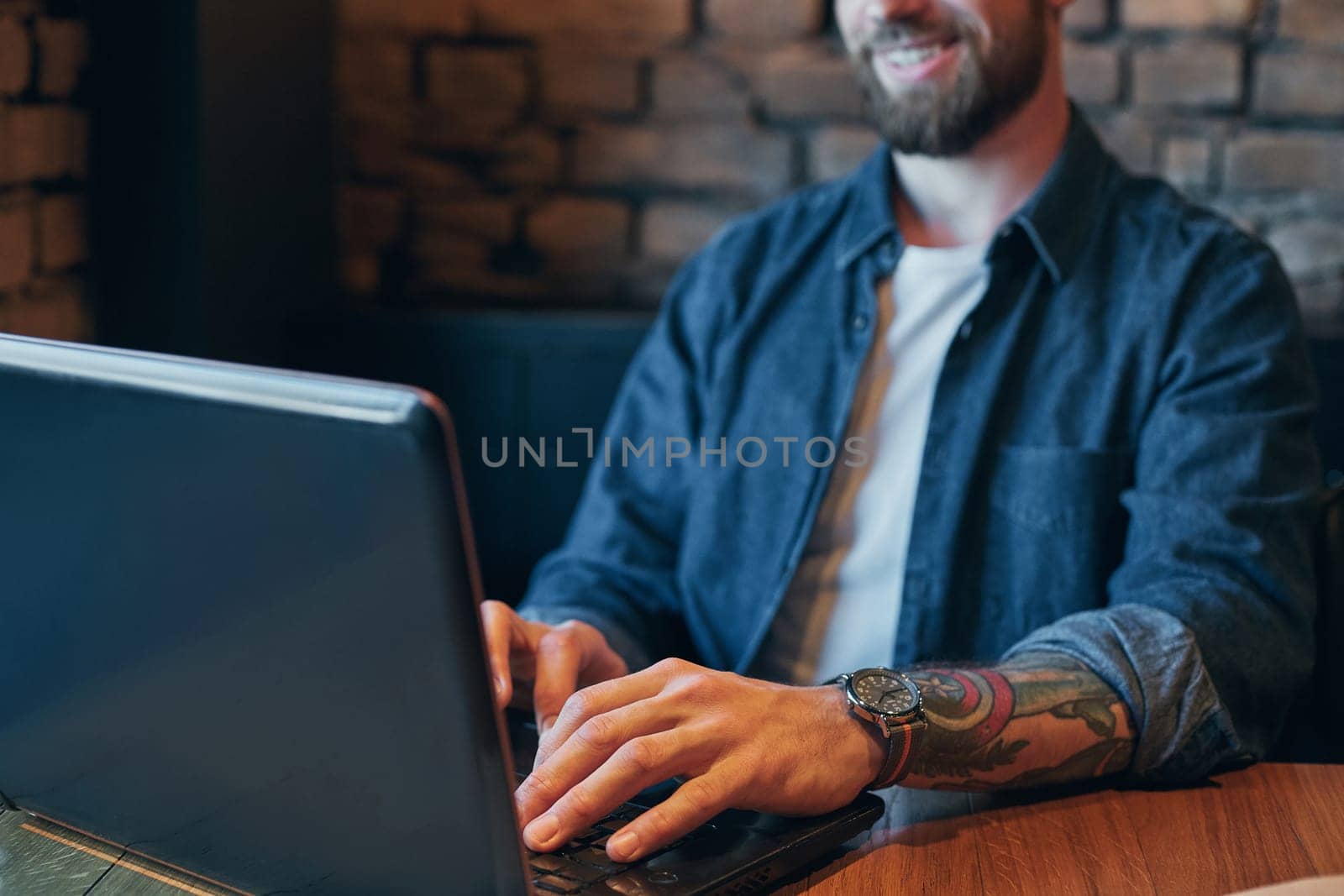 Young hipster guy at the bar having a cappuccino. Young man drinking coffee in city cafe during lunch time and working on laptop. Close up