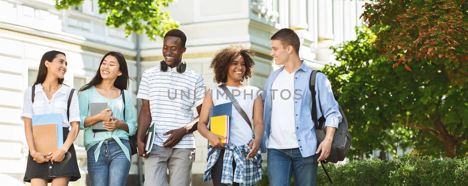 Students communication. Group of college friends walking outdoors in university campus, resting after classes, chatting and laughing, free space