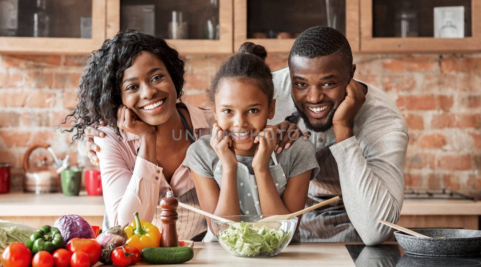 Adorable afro family cooking healthy dinner together at kitchen, posing at camera, making salad, copy space