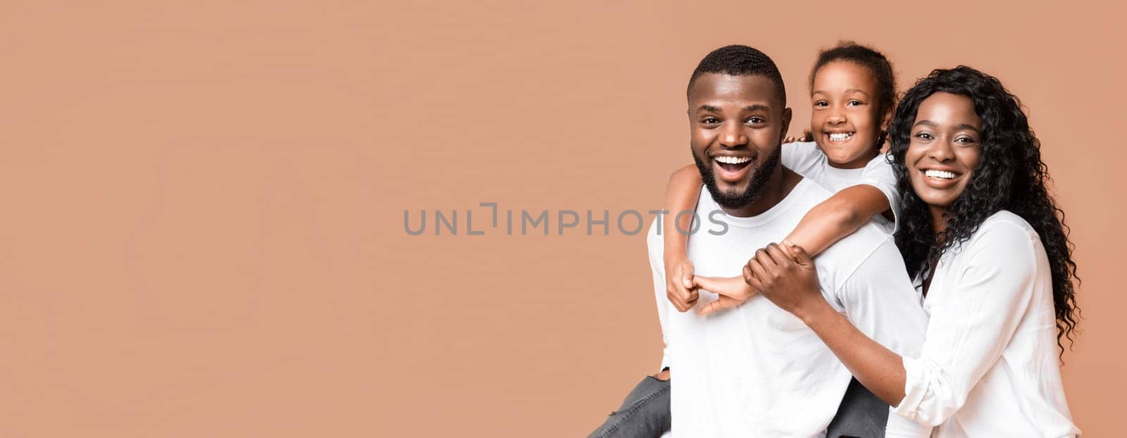 Family fun. Young african american parents spending time with their little daughter, laughing together over yellow background
