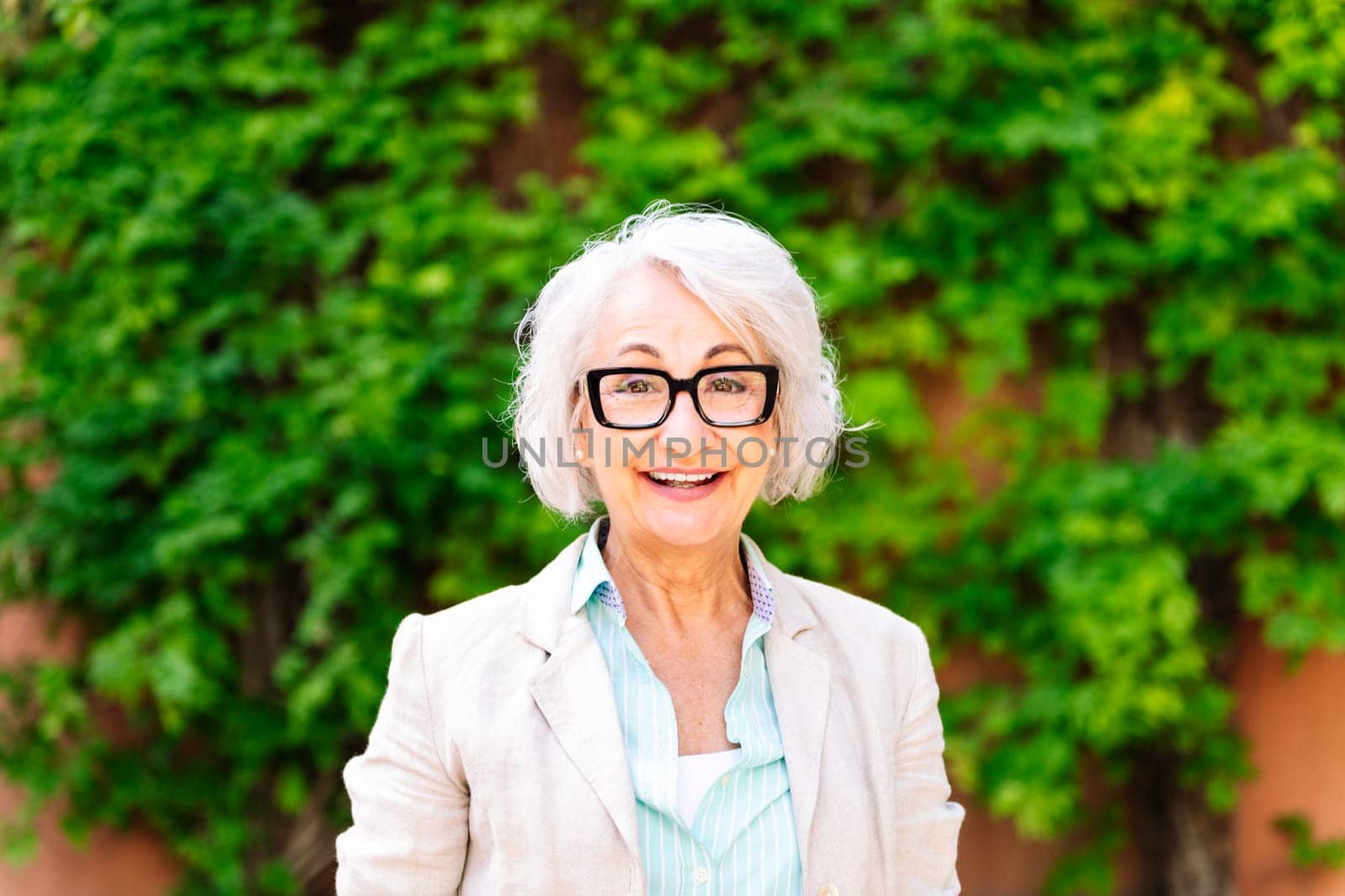 portrait of a middle age woman smiling happy looking at camera with blurred green plants background, concept of mature people lifestyle