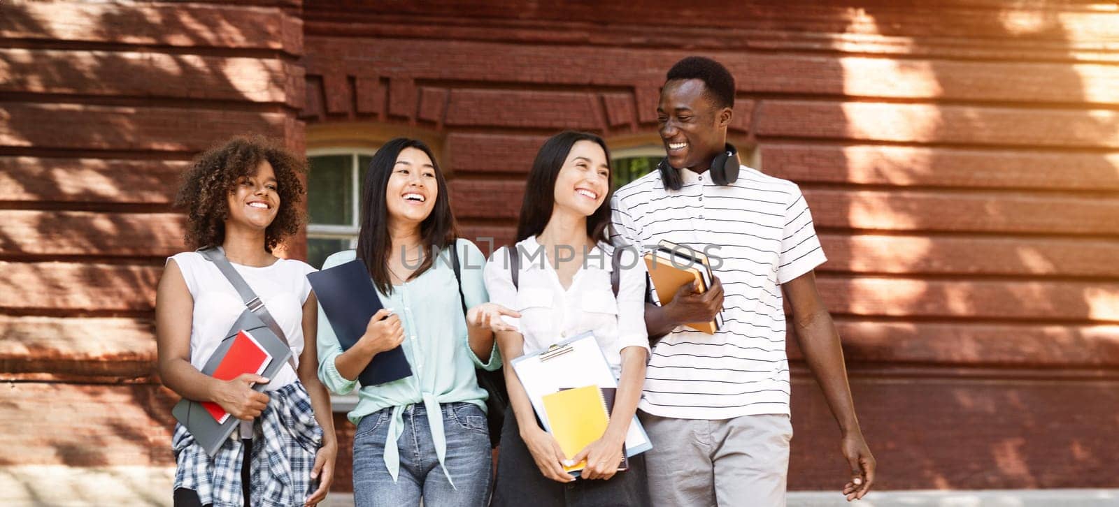 Group of happy students walking in university campus, chatting and laughing during break, copy space