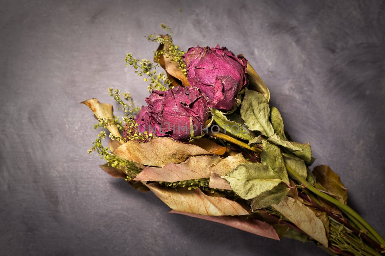 A studio photo of a bouquet of dried red roses on a table.