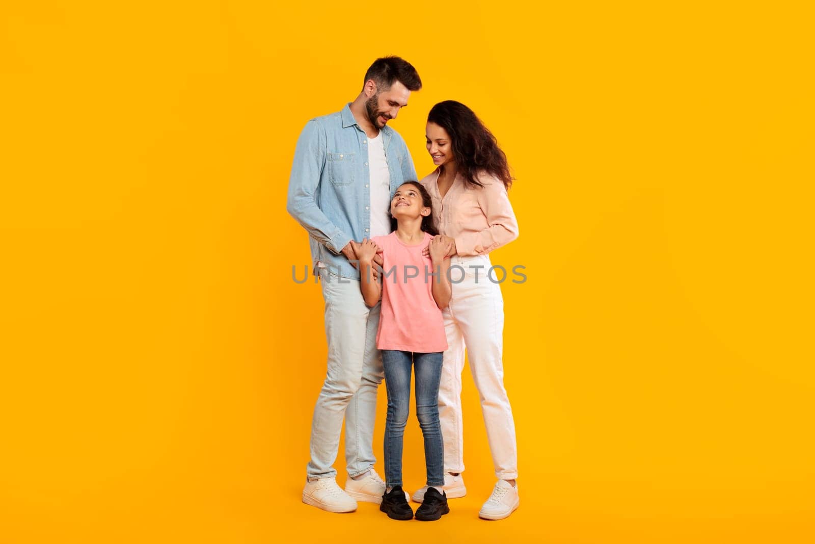 A happy family stands together in front of a yellow background, smiling at each other. They all have smiles on their faces and look happy to be together.