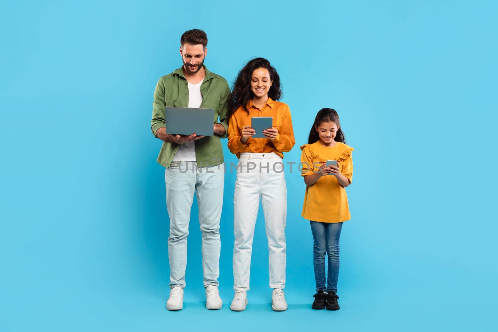 A man, woman, and young girl stand in a row against a light blue background. Family using various devices. Gadgets addiction