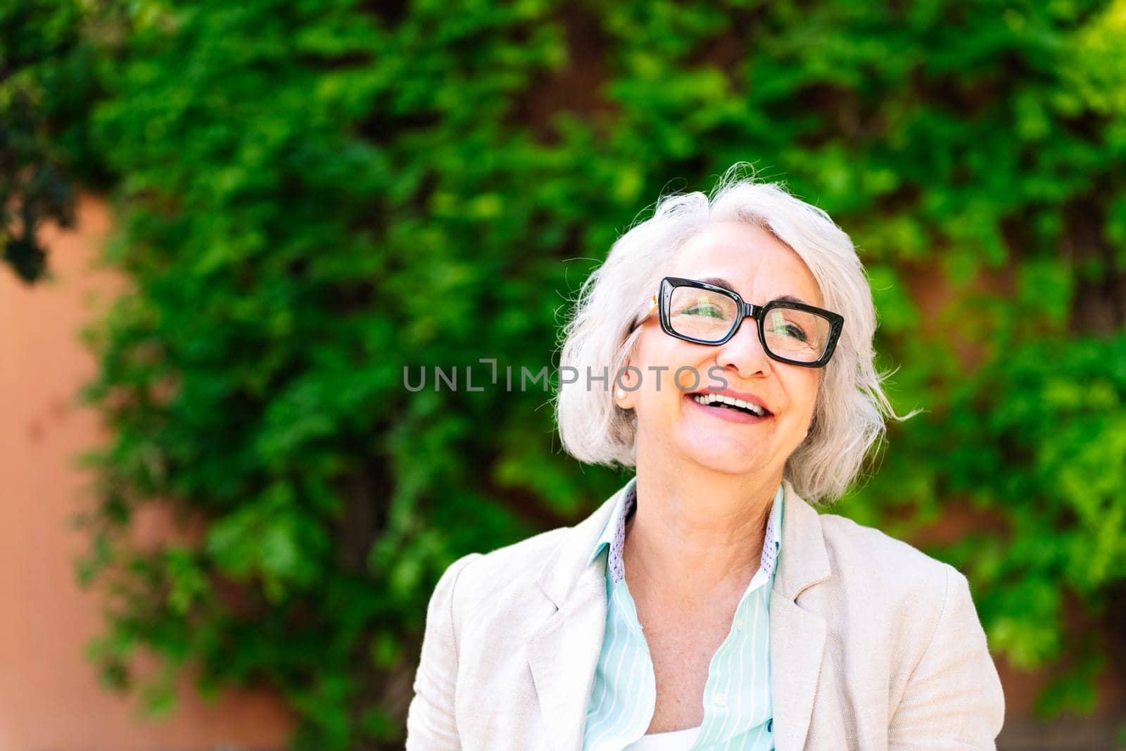 portrait of a middle age woman laughing happy with blurred green plants background, concept of mature people lifestyle, copyspace for text