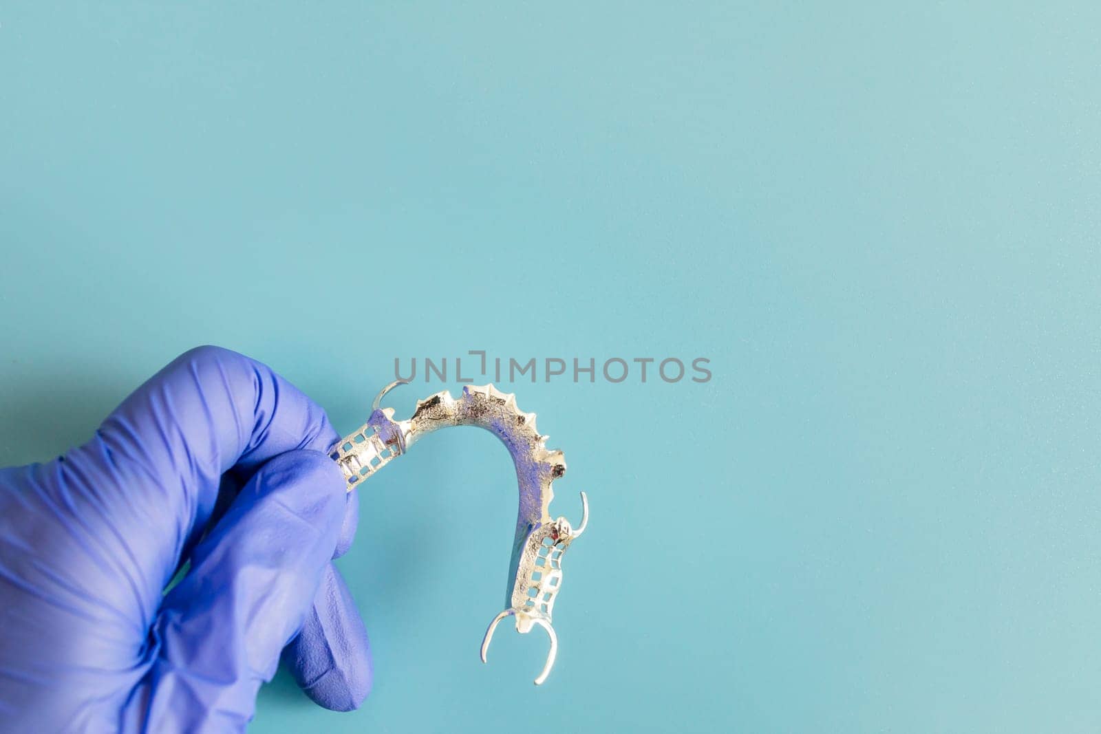Mockup Metal Frame Lower Partial Denture, Cobalt Chrome Dental Plate, Bridge Printed By 3d Printer in Doctor's Hand. Blue Background. Flat Lay Mockup. Copy Space For Text. Dentistry. Horizontal Plane