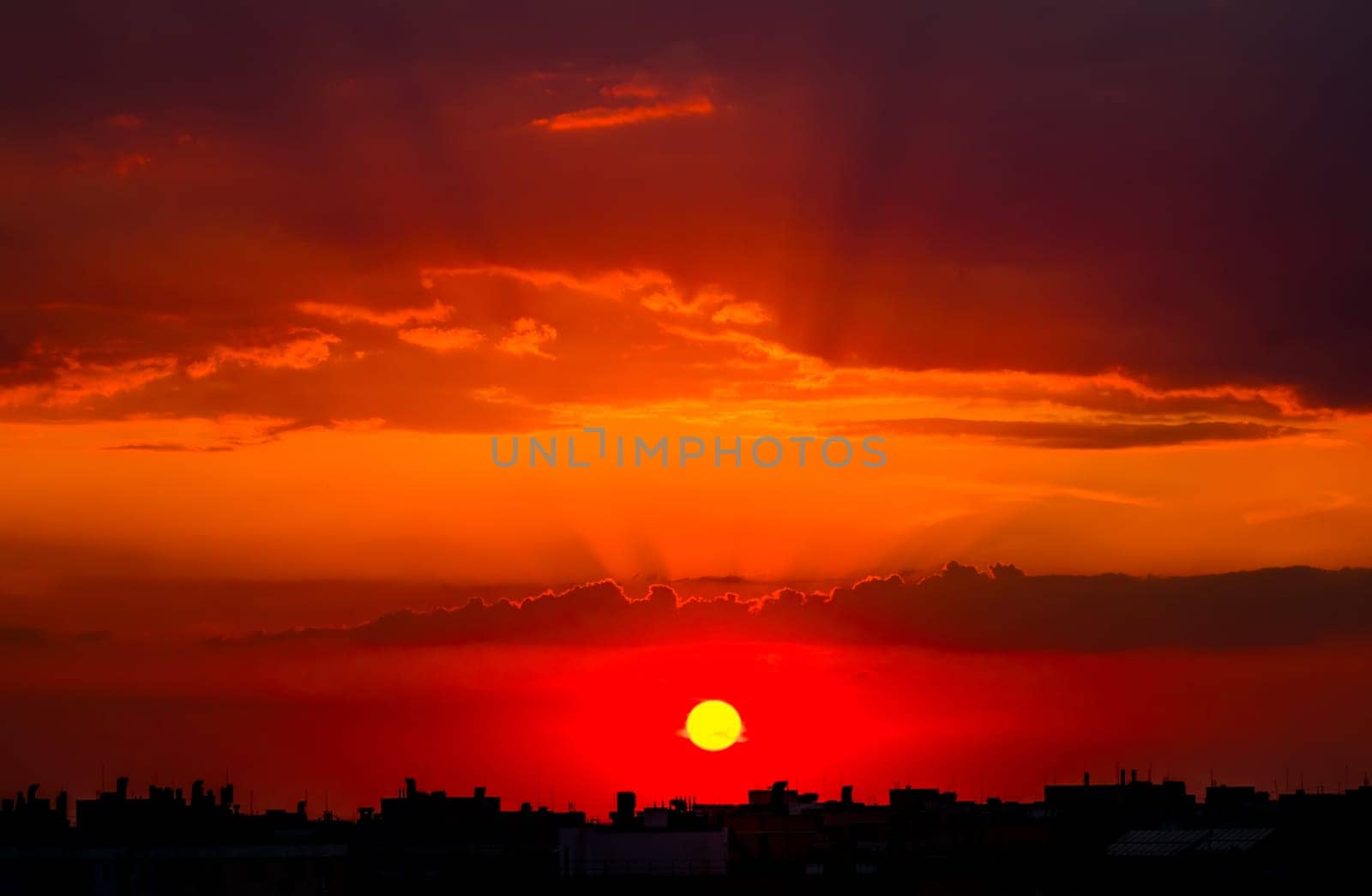 Cloudy sky above the city rooftops. The rays of the setting sun paint the sky a rich red color