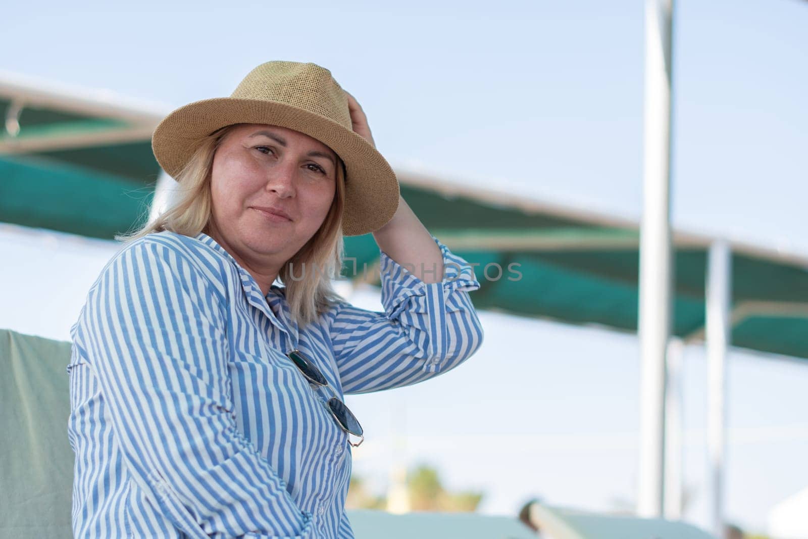 Young woman sitting on a sun lounger on the beach wearing a hat, looking tense, unable to relax even on vacation, deep in thought, midlife crisis