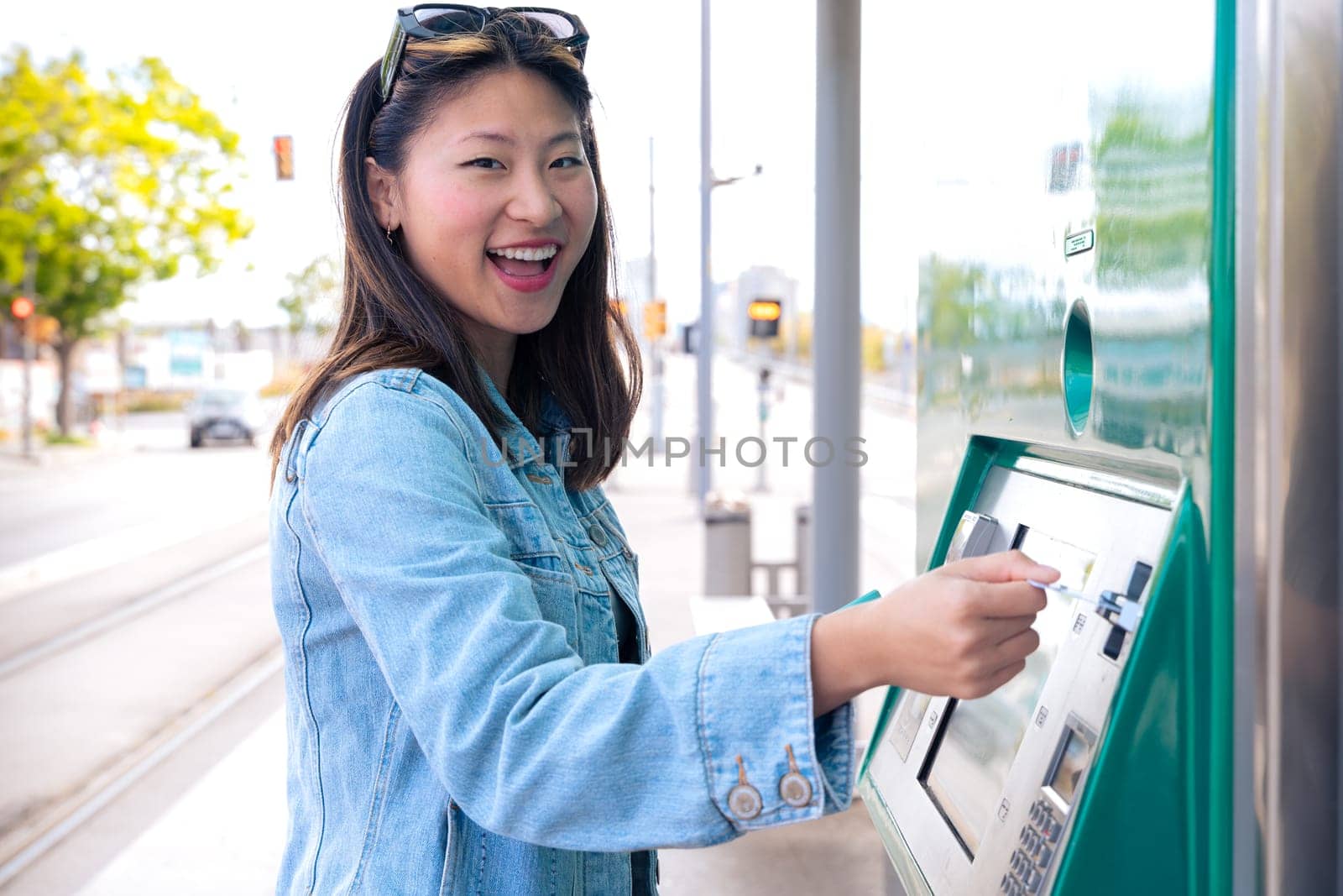 Young beautiful Chinese woman buying metro ticket at vending machine in Barcelona metro station looking at camera.invisalign