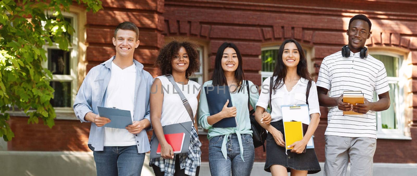 Happy multicultural students walking near university campus together, soending time outdoors after classes, free space
