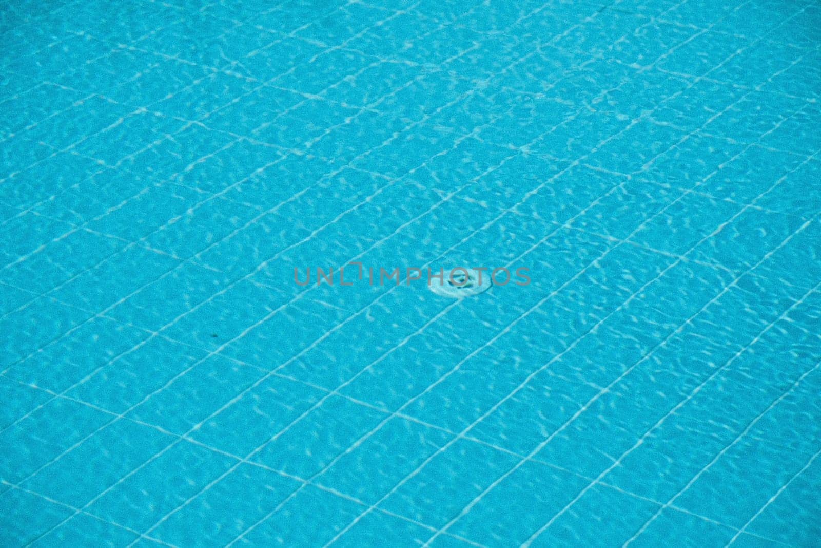 Defocused blurred transparent blue clear calm swimming pool water surface texture and water drain hole on the bottom, abstract background, place for text,