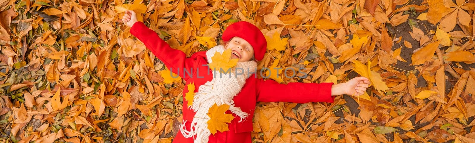 An overhead view of a caucasian girl in a red coat and beret lies on yellow foliage. Walk in the park in autumn. Widescreen. by mrwed54