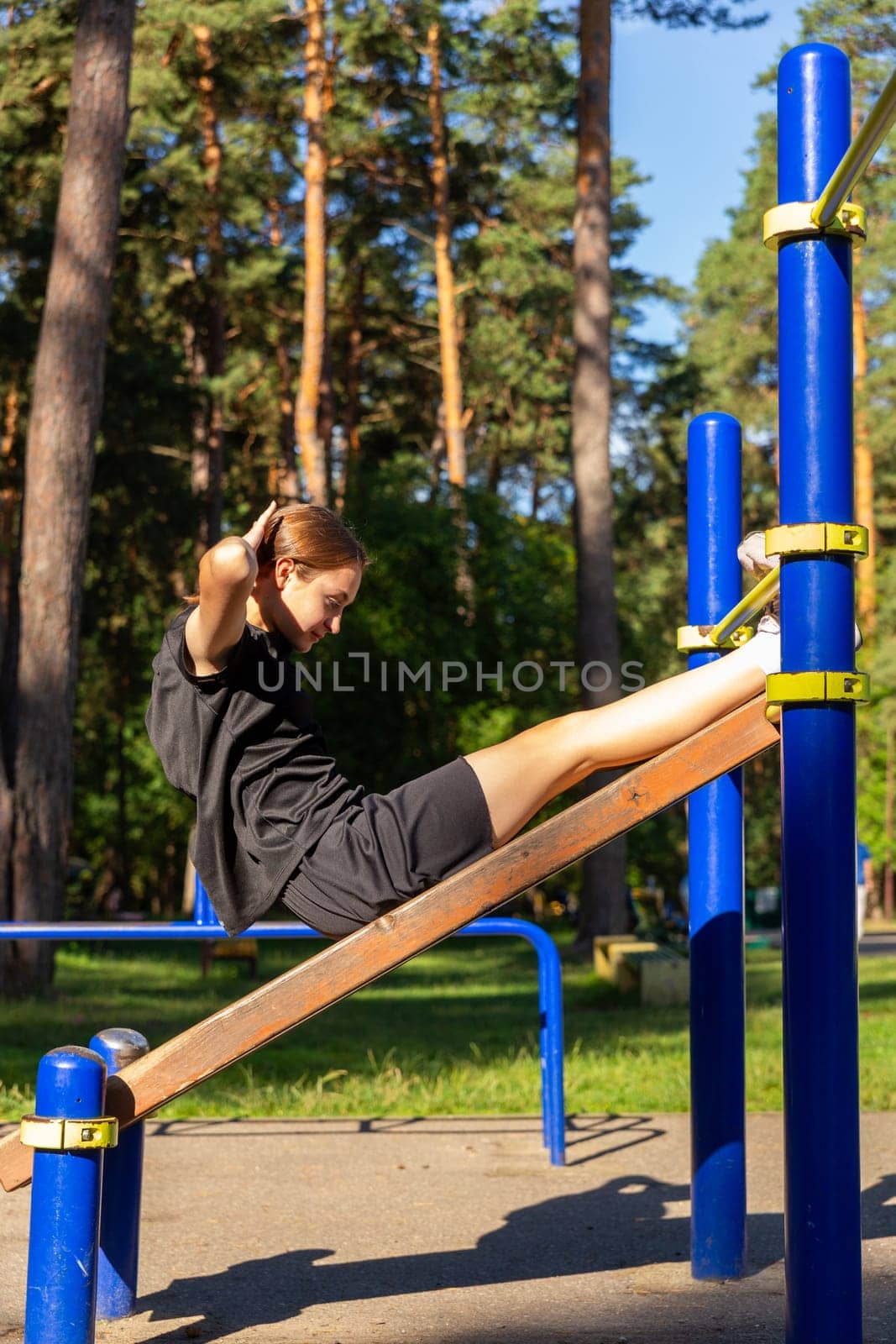 A teenage girl doing abdominal crunches. A girl performs exercises for the development of core muscles on a training ground in a city park