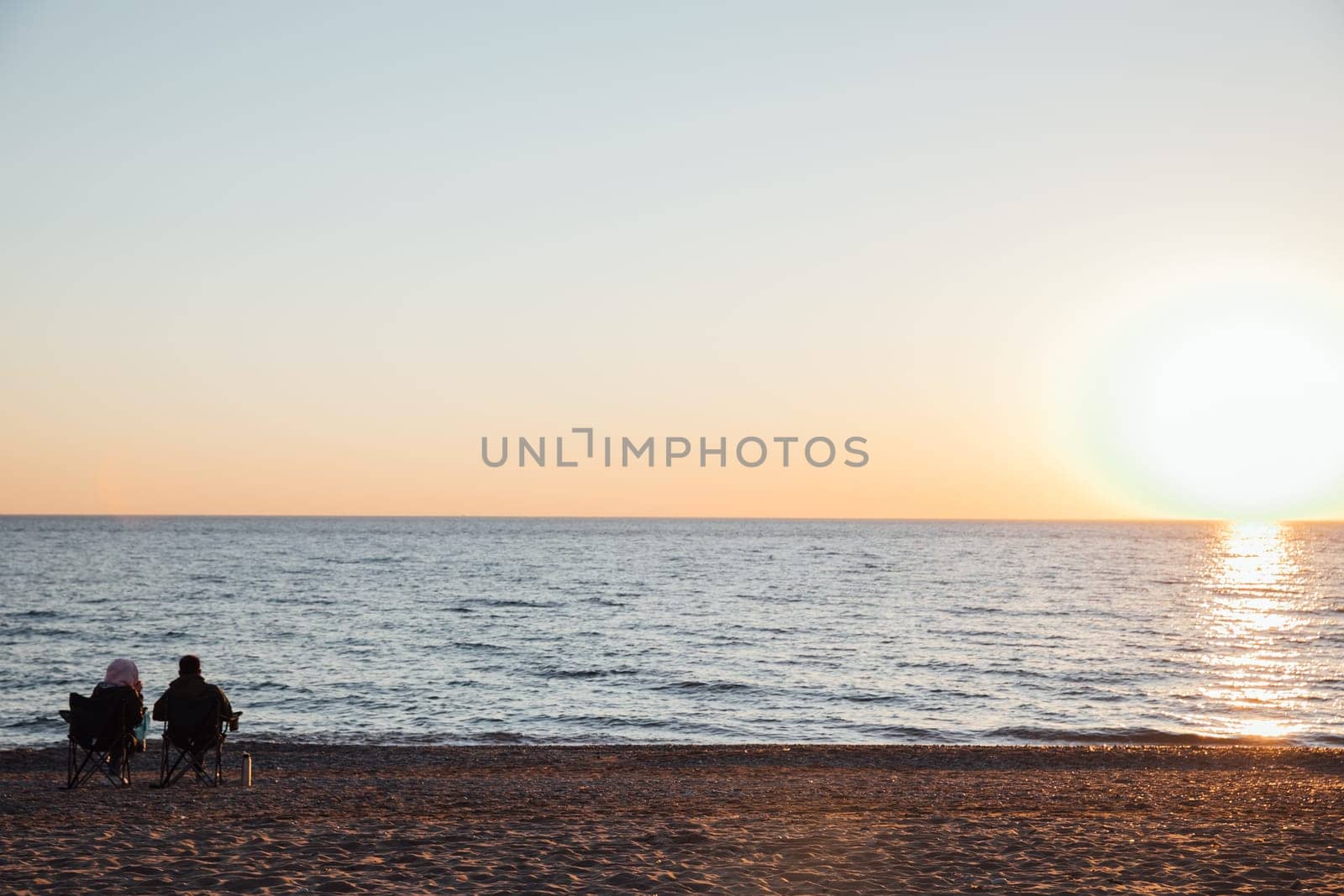 sea shore beach at sunset two people sitting on chairs by Simakov
