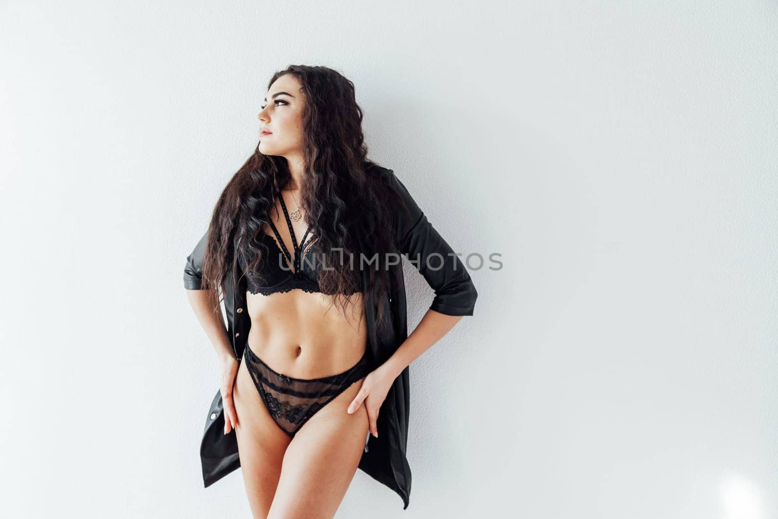 brunette woman in black underwear stands against a white wall