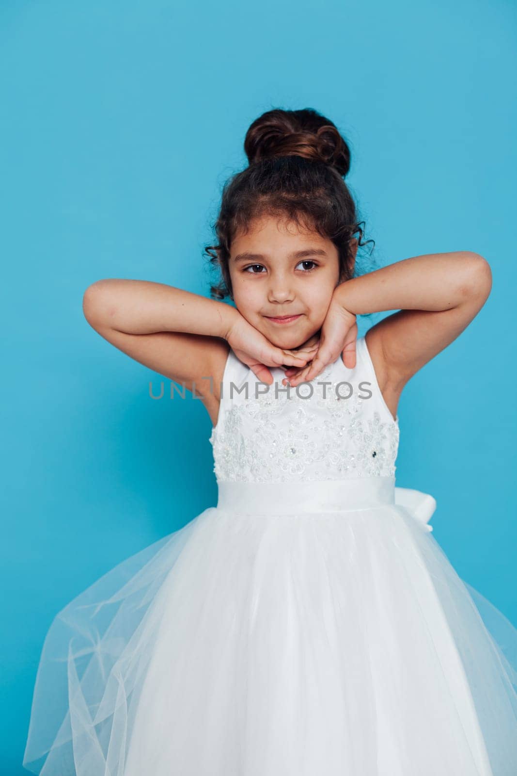 a little girl in white dress with a hairstyle poses on a blue background