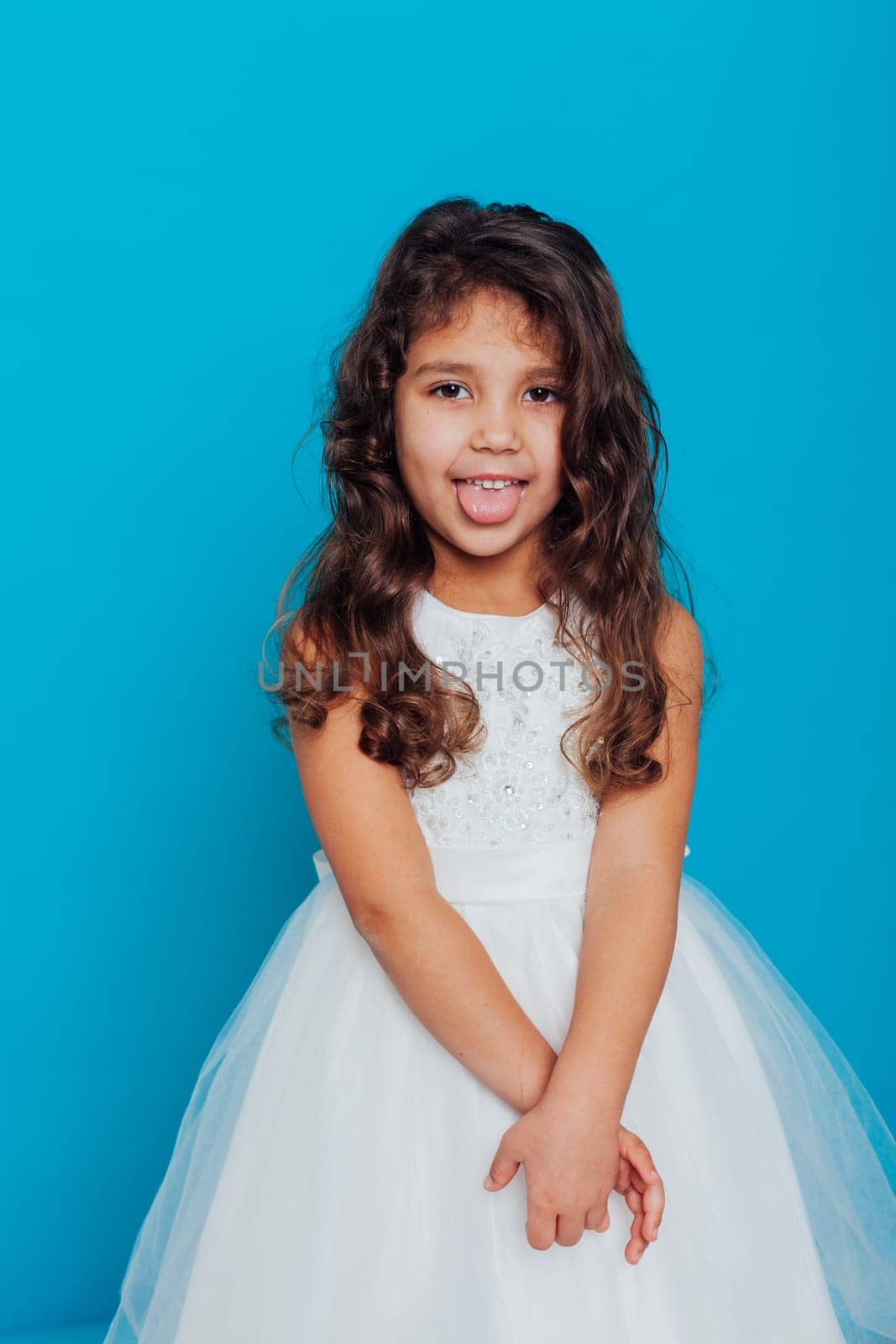 little girl in a white dress shows her tongue on a blue background