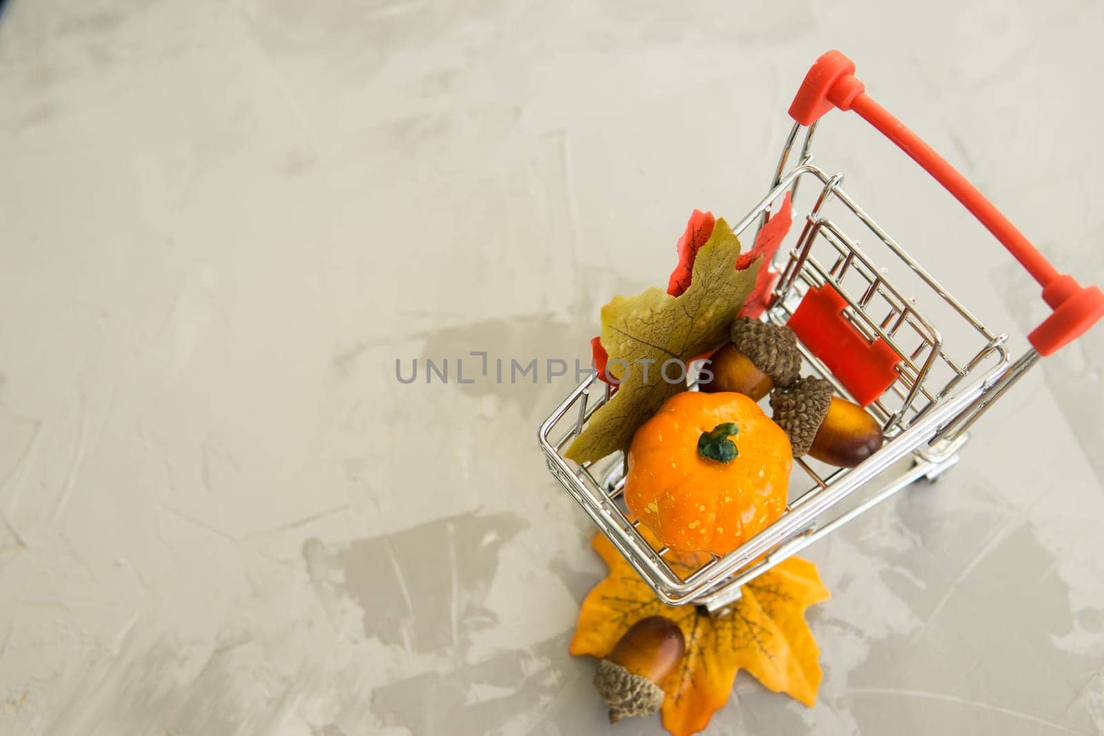 Grocery cart with decorative pumpkins and maple leaves on a concrete background. The concept of the autumn sales. Black Friday and cyber Monday. Space for text.
