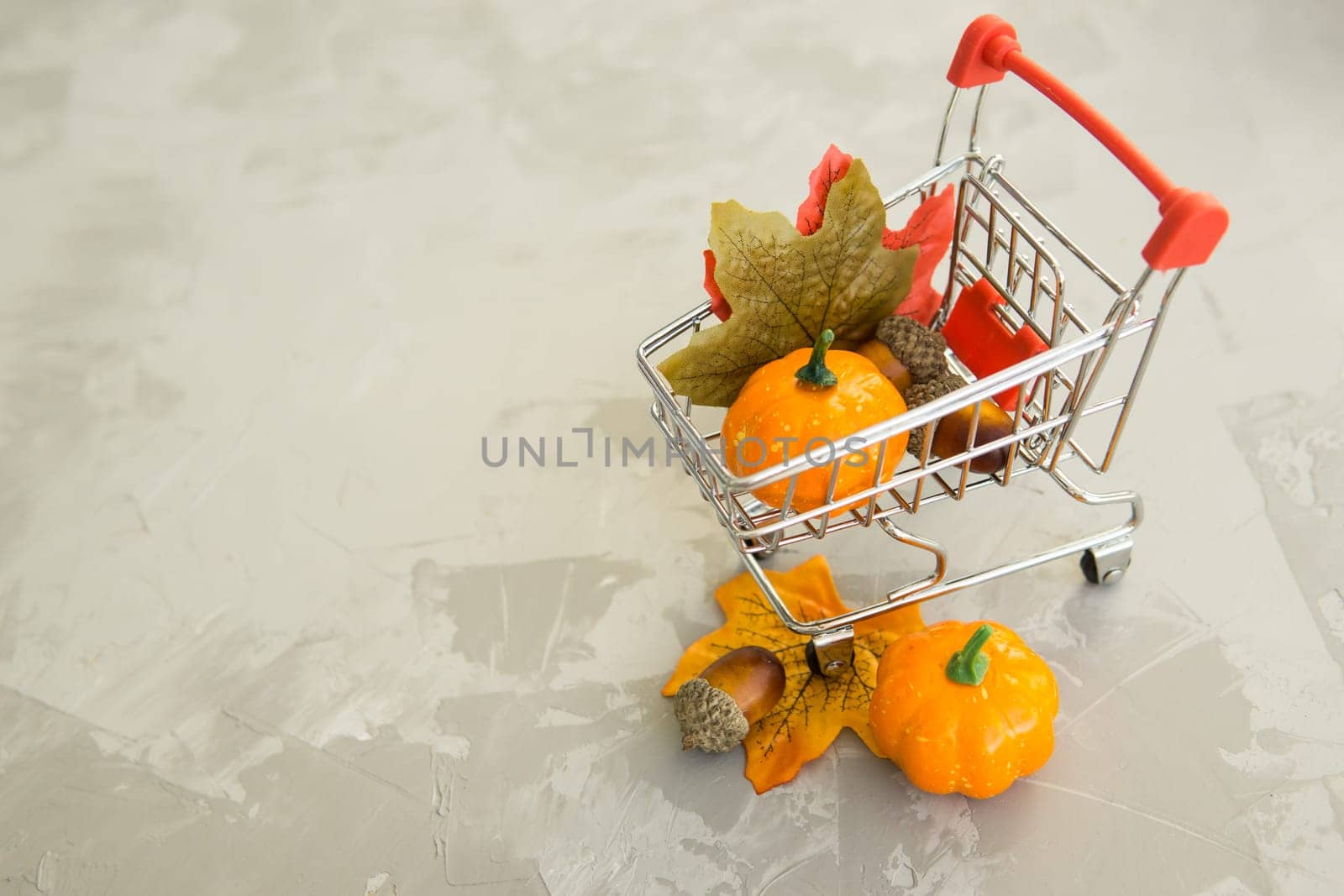 Grocery cart with decorative pumpkins and maple leaves on a concrete background. The concept of the autumn sales. Black Friday and cyber Monday. Space for text.