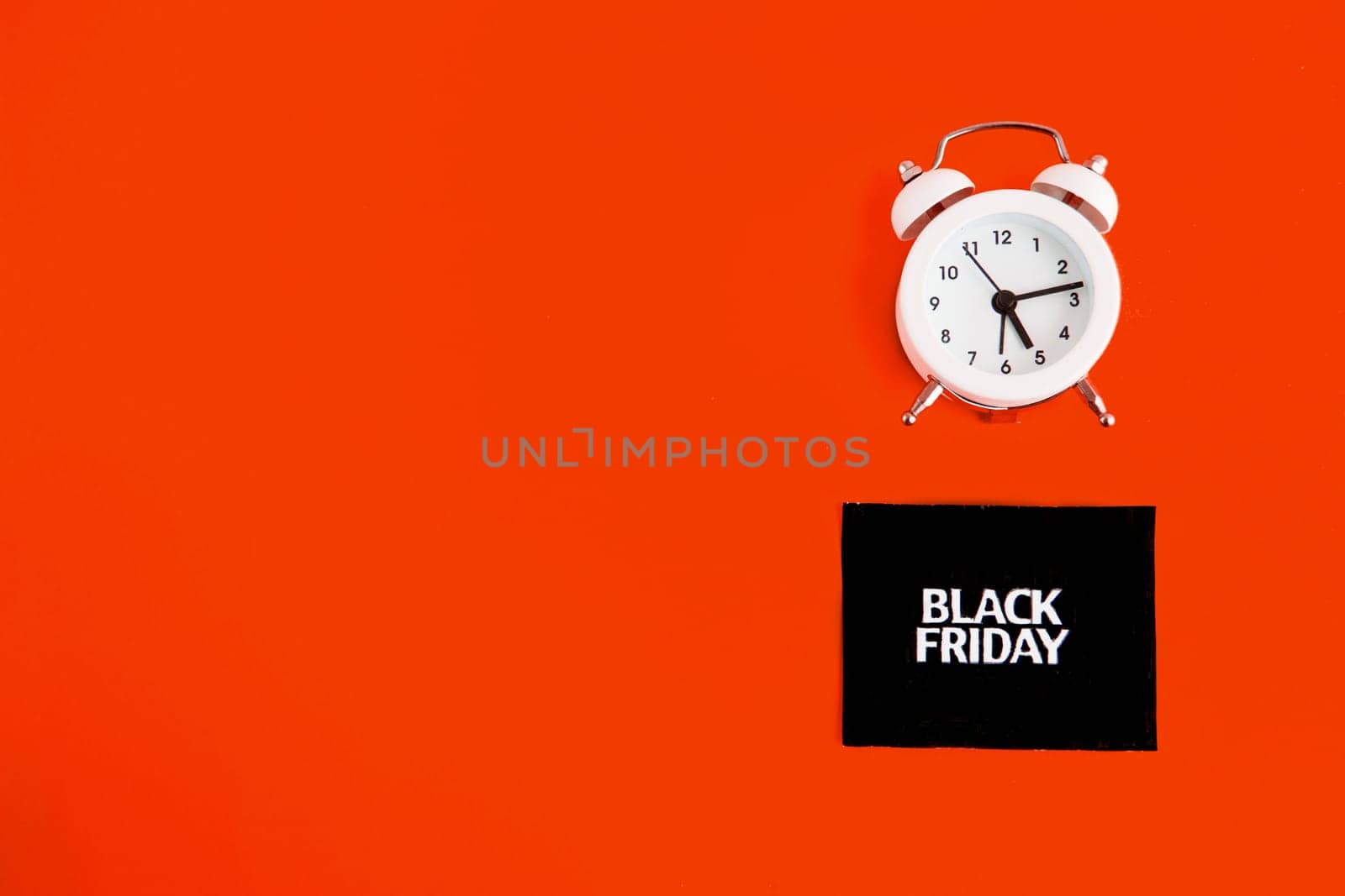 white alarm clock and an inscription on a black square - black Friday on a red background. The topic of sales. Flat lay.