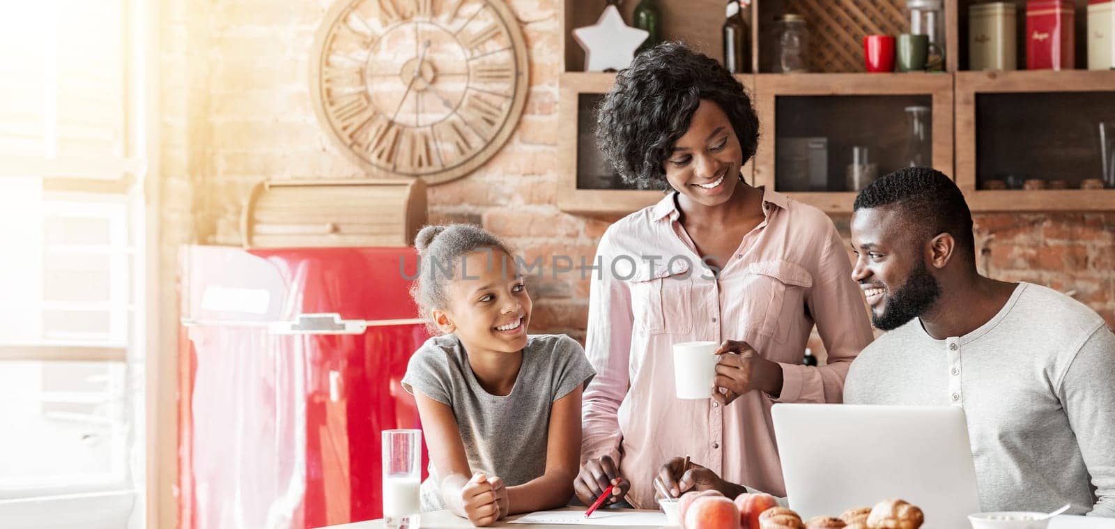Positive afro family planning day in the morning during breakfast in kitchen, using laptop, copy space
